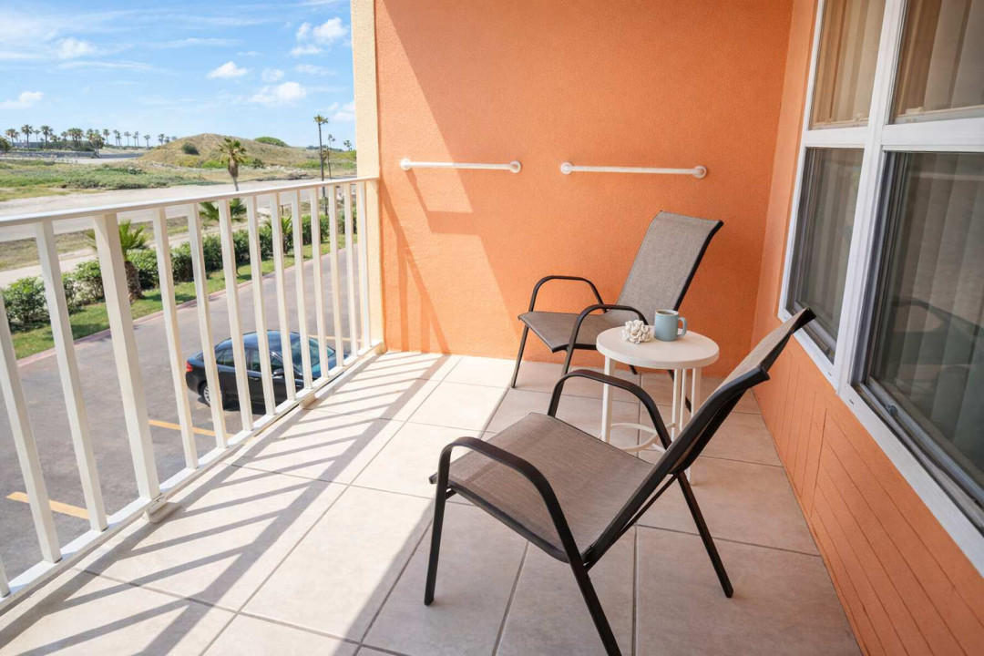 Sunlit balcony with palm view, mesh chairs, and accessibility features—perfect for morning coffee or evening breeze. Close to beach, parking, and tropical greenery.