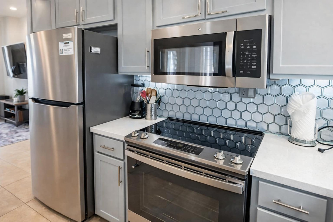 Modern coastal kitchen featuring stainless steel appliances, sleek gray cabinetry & a hexagonal tile backsplash. Bright, inviting space ideal for cooking & entertaining, blending functionality with contemporary design for a premium rental experience.
