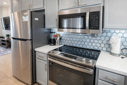 Modern coastal kitchen featuring stainless steel appliances, sleek gray cabinetry & a hexagonal tile backsplash. Bright, inviting space ideal for cooking & entertaining, blending functionality with contemporary design for a premium rental experience.