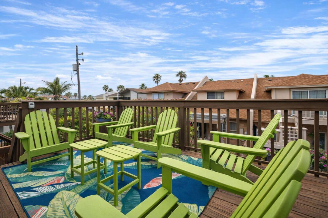 Tropical deck retreat with 6 vibrant Adirondack chairs, lush palm views, and colorful rug—perfect for morning coffee or sunset chats in a coastal neighborhood. Relax, unwind, and soak in the beachside vibes.