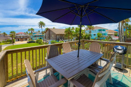 Relax and dine outdoors on the private deck, featuring a stylish table set for six, a large umbrella for shade, and a grill for barbecues—perfect for enjoying coastal breezes and neighborhood views.