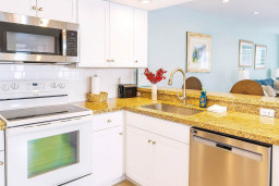 Bright Coastal Kitchen Granite Counters & Stainless Appliances.
Spacious white cabinetry, gold-flecked granite, microwave/oven/dishwasher shine under soft light. Red flowers, beach art & bar stools invite family meals—cook up vacation magic in style.