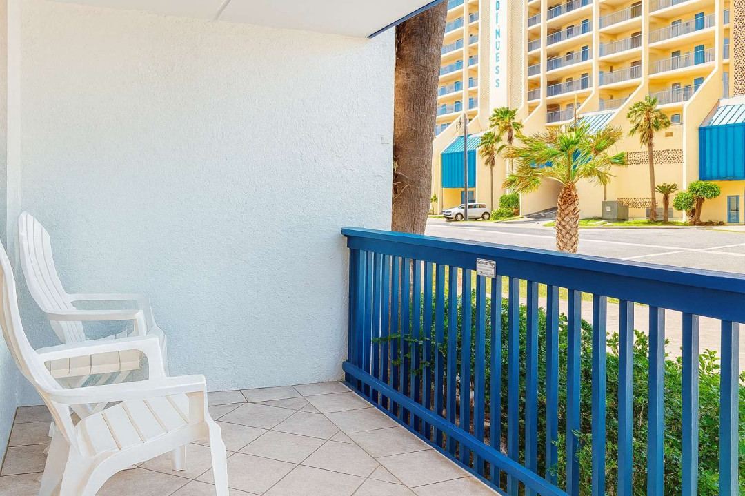 Serene White Balcony
Adirondack Chairs Over Palm-Lined Complex. Crisp stucco terrace w/ blue railings & 2 comfy white chairs overlooks swaying palms, parked cars & beige high-rise. Breezy spot for sunset cocktails & people-watching in coastal haven!