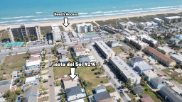 Aerial view of a vibrant coastal community with sandy shoreline, nearby amenities, and easy beach access. A prime location that offers guests convenience, walkability, and a relaxed seaside atmosphere perfect for effortless vacation living.