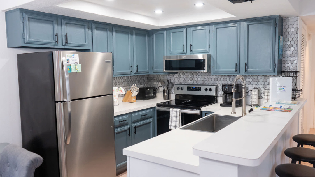 Modern kitchen with blue‑gray cabinetry, stainless appliances, and a bright island workspace. Patterned tile backsplash and thoughtful essentials create a clean, functional space perfect for cooking, gathering, and effortless vacation living.