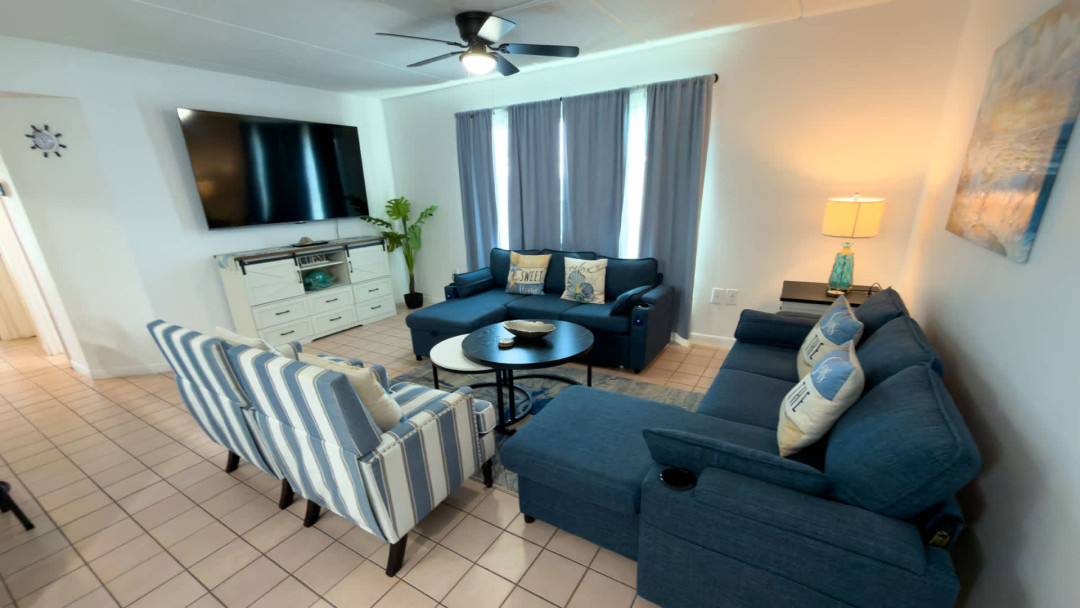 Bright coastal living room with comfortable sofa, striped armchairs, and beach‑inspired pillows. Soft blue tones, natural textures, and open sightlines create a relaxing, welcoming space perfect for unwinding after a day of island adventures.