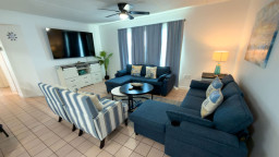 Bright coastal living room with comfortable sofa, striped armchairs, and beach‑inspired pillows. Soft blue tones, natural textures, and open sightlines create a relaxing, welcoming space perfect for unwinding after a day of island adventures.