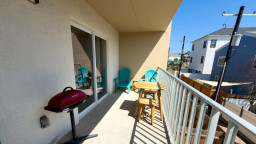 Sunny balcony with turquoise Adirondack chairs, a bistro set, and a convenient grill. Bright, breezy, and perfect for morning coffee or evening downtime, this outdoor space offers guests a relaxing spot to unwind and enjoy coastal vacation living.