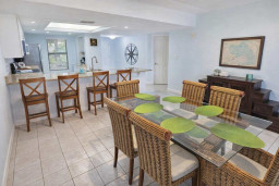 Spacious kitchen & dining area with glass-top table, wicker chairs, breakfast bar, white cabinetry, and pet-friendly touches. Bright, clean, and perfect for family stays or group getaways near the coast.