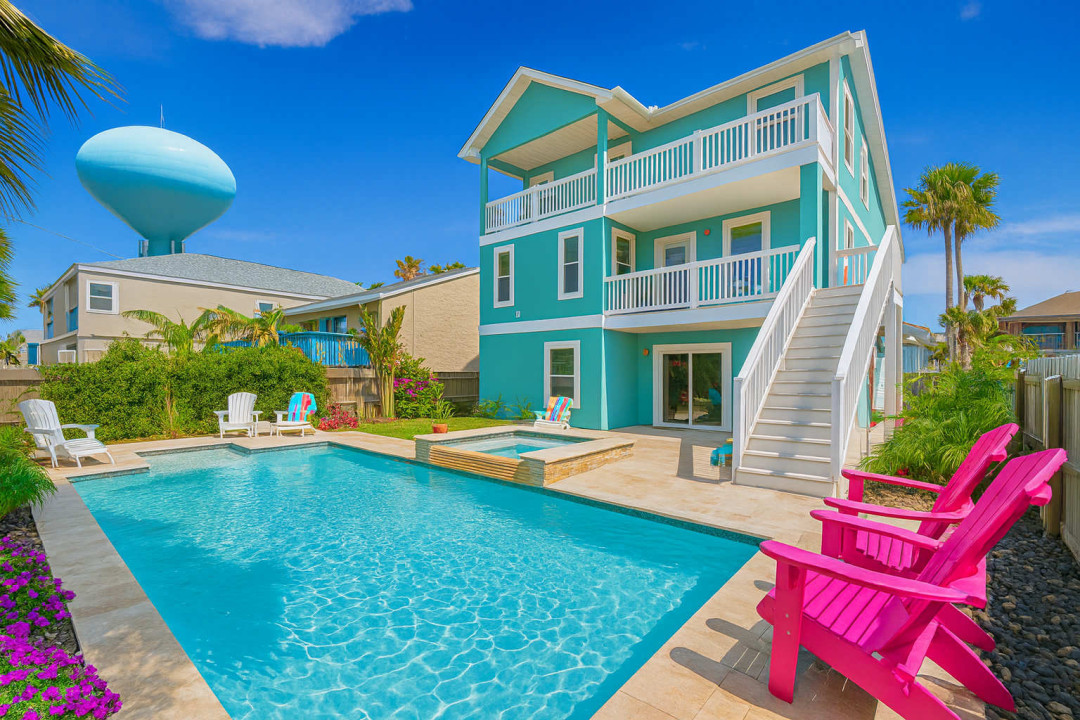 This charming three-story beach house features vibrant turquoise exterior, spacious balconies, and a sparkling swimming pool surrounded by lounge chairs. Perfect for a relaxing getaway with stunning ocean views and ample outdoor entertainment space.