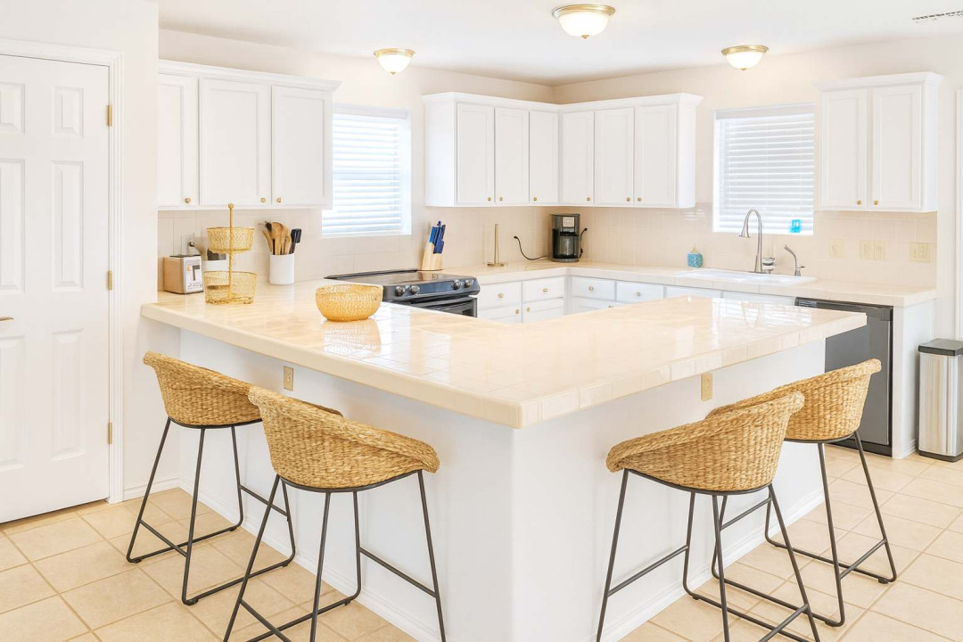 Bright, inviting kitchen featuring ample counter space, sleek white cabinetry, and modern appliances. Enjoy casual dining at the spacious breakfast bar with stylish wicker stools—perfect for morning coffee or entertaining guests in comfort.