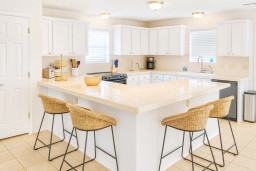 Bright, inviting kitchen featuring ample counter space, sleek white cabinetry, and modern appliances. Enjoy casual dining at the spacious breakfast bar with stylish wicker stools—perfect for morning coffee or entertaining guests in comfort.
