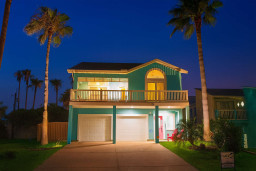 Welcome to this stunning turquoise beach house, perfectly lit for evening relaxation. Enjoy spacious balconies, double garage, lush palm landscaping, and a stylish pink front door—ideal for coastal living just steps from the shore!