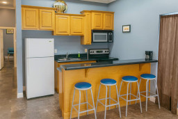 Cozy Breakfast Bar Kitchen
Whip up meals in the fully stocked kitchen with wood cabinets, white fridge, stove, microwave, double sink, and black granite counters. Four blue barstools create a casual breakfast bar hangout.