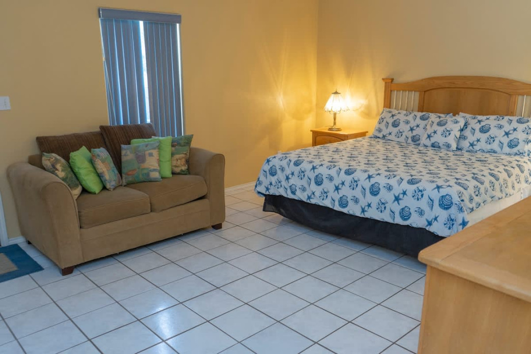 Master bedroom with a plush queen bed, soft lighting, and a comfy loveseat—creating a warm, relaxing space perfect for unwinding after a day of island adventures.