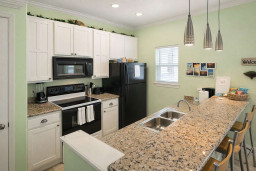 Bright, modern kitchen with granite countertops, stainless steel sink, black appliances, and pendant lighting—perfect for cooking, entertaining, or enjoying a morning coffee at the breakfast bar.