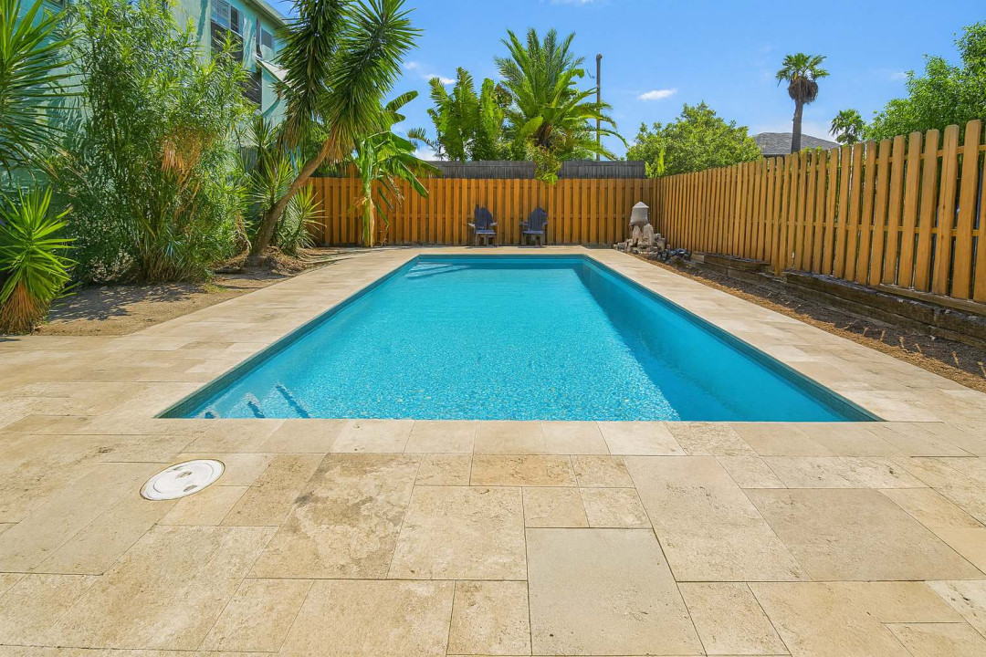 A calm backyard escape with a sunlit pool framed by warm stone and tropical greens, offering an easygoing spot to unwind, stretch out by the water, and enjoy slow, open‑air moments in a relaxed setting that feels naturally inviting.