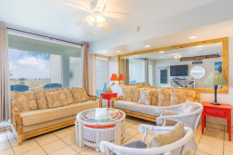 Bright Coastal Living Room with Tropical Flair & Patio Views
Relax in this airy beachside living room with bamboo and wicker furniture, tropical accents & patio views. Features include a flat-screen TV, ceiling fan, mirrored wall, and vibrant decor.