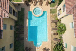 Stylish poolside retreat with tub, tropical landscaping, and lounge seating—perfect for relaxing under the sun between two charming Mediterranean-style villas.