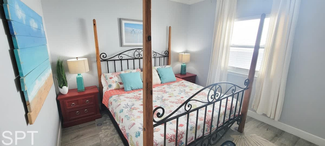 Bright and inviting primary bedroom featuring a wrought‑iron canopy bed, floral linens, turquoise accents, and abundant natural light — a relaxing retreat designed for comfort and style.