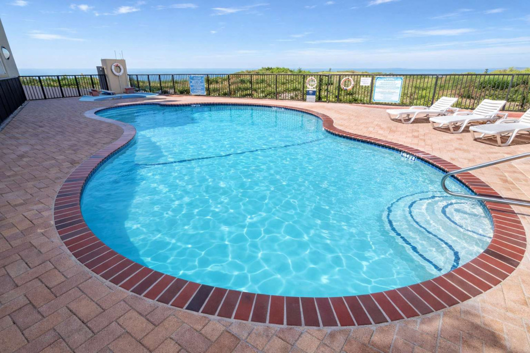 Sunlit pool retreat framed by brick and coastal breeze — a serene escape where calm water meets open sky. Perfect for unwinding after beach days or morning swims, this space invites effortless relaxation and genuine vacation moments.