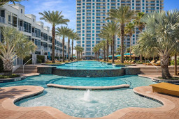 Luxurious resort-style pool retreat with cascading water features, tropical landscaping, and high-rise views—perfect for relaxing under palm trees and soaking up the sun in a vibrant coastal setting.