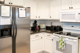 Bright Coastal Kitchen w/ Stainless Essentials. Spacious white cabinetry frames stainless fridge, smooth-top range, microwave & deep sink amid granite counters, coffee station & tiled floors. Fully equipped for whipping up beachy meals with ease.