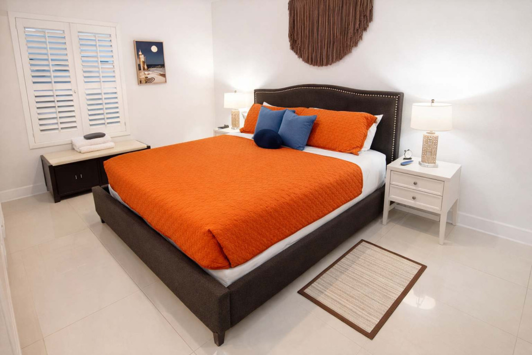 A bright, modern retreat with warm tones and coastal charm. The inviting orange bedspread and soft blue accents create a relaxed, stylish space perfect for unwinding after a sun‑filled day near the shore.