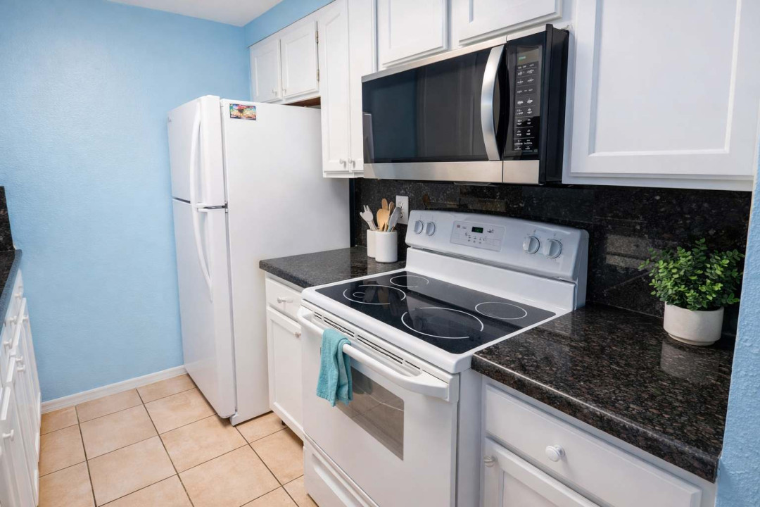 A compact, coastal‑bright kitchen where simplicity meets comfort — crisp white cabinetry, dark granite contrast, and soft blue walls create a clean, inviting vibe perfect for easy mornings and relaxed evenings in your South Padre getaway.