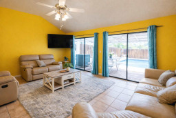 Bright, inviting living space with cheerful yellow tones and soft leather seating. Sunlight pours through glass doors leading to a sparkling pool, creating a relaxed coastal feel perfect for unwinding after island adventures.