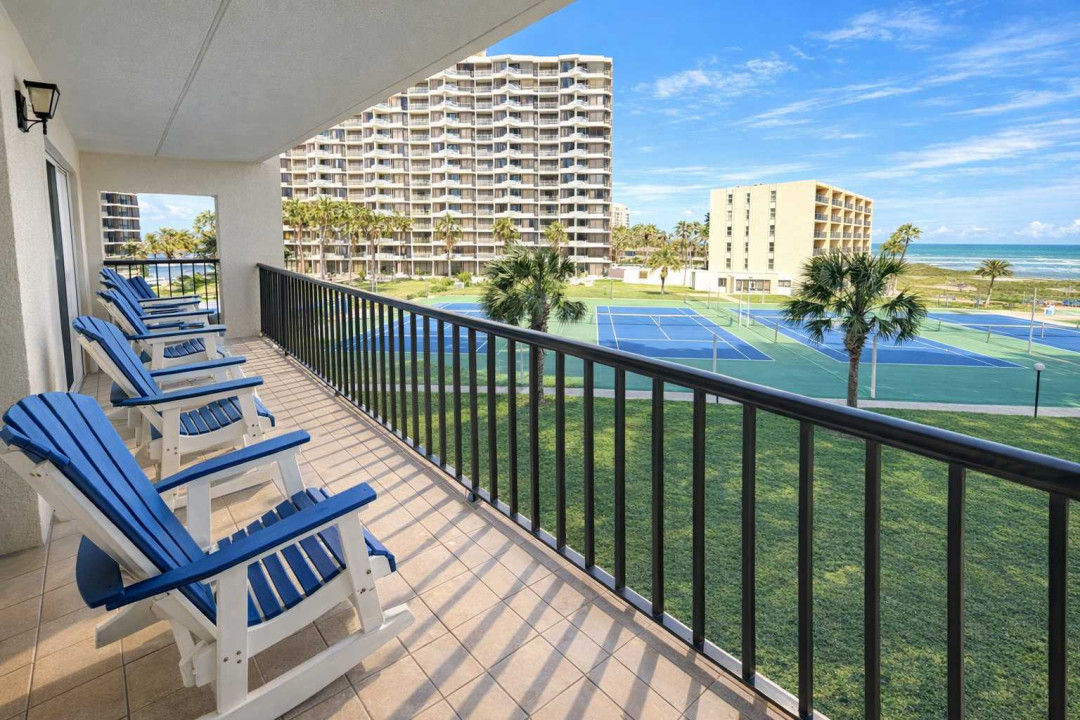 Oceanview Balcony with Tennis Courts & Resort Amenities – Relax in Blue Adirondack Chairs Overlooking Palm Trees, Coastal Breeze, and Sunny Skies. Perfect for Beach Getaways, Family Fun, and Active Retreats.