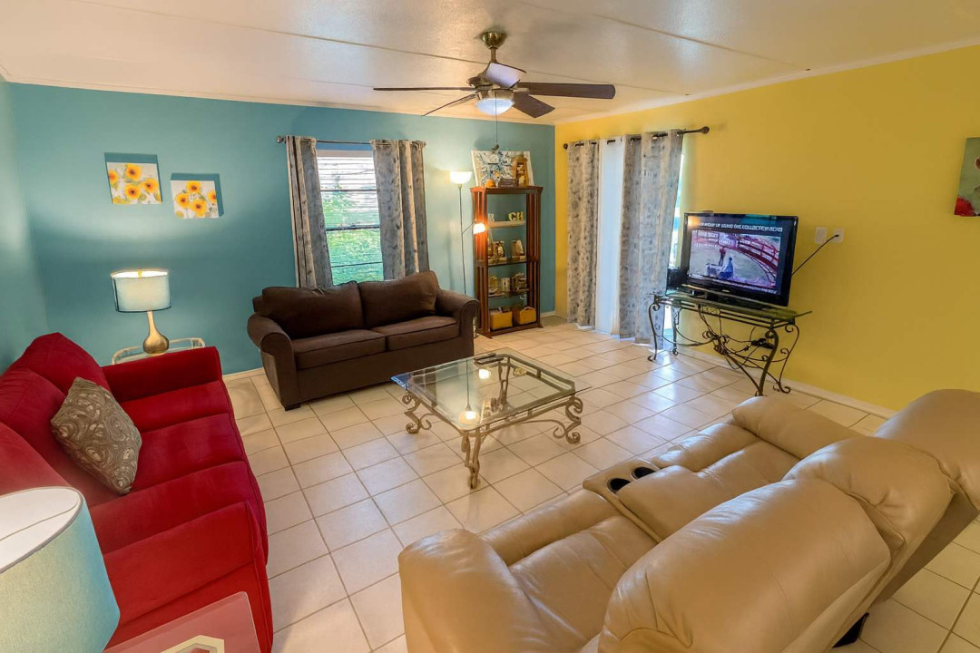 Relax in this colorful living room featuring cozy seating, a flat-screen TV, plenty of natural light. with vibrant décor, ceiling fan, and direct access to the patio, it’s the perfect space to unwind after a day at the beach or exploring the island.