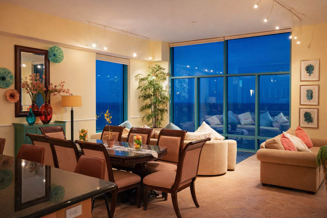 Modern beachfront condo with stunning ocean views, stylish dining for 8, cozy seating, vibrant decor, and floor-to-ceiling windows—perfect for relaxing or entertaining at sunset.