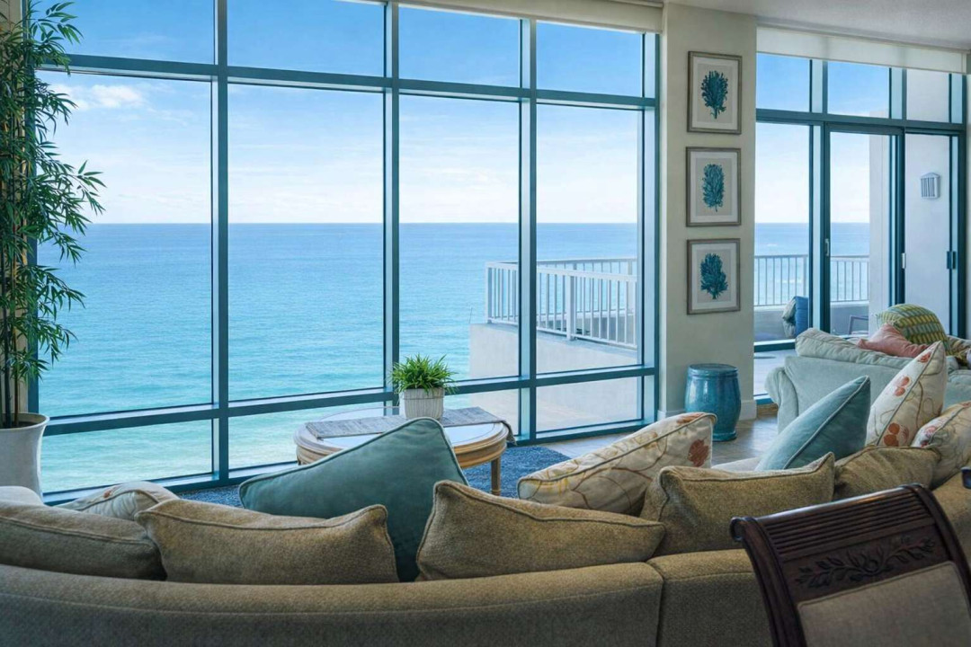 Oceanfront Living Room with Panoramic Views — Spacious, sunlit interior featuring floor-to-ceiling windows, coastal décor, and direct balcony access overlooking the sea. Ideal for relaxing getaways and scenic stays.