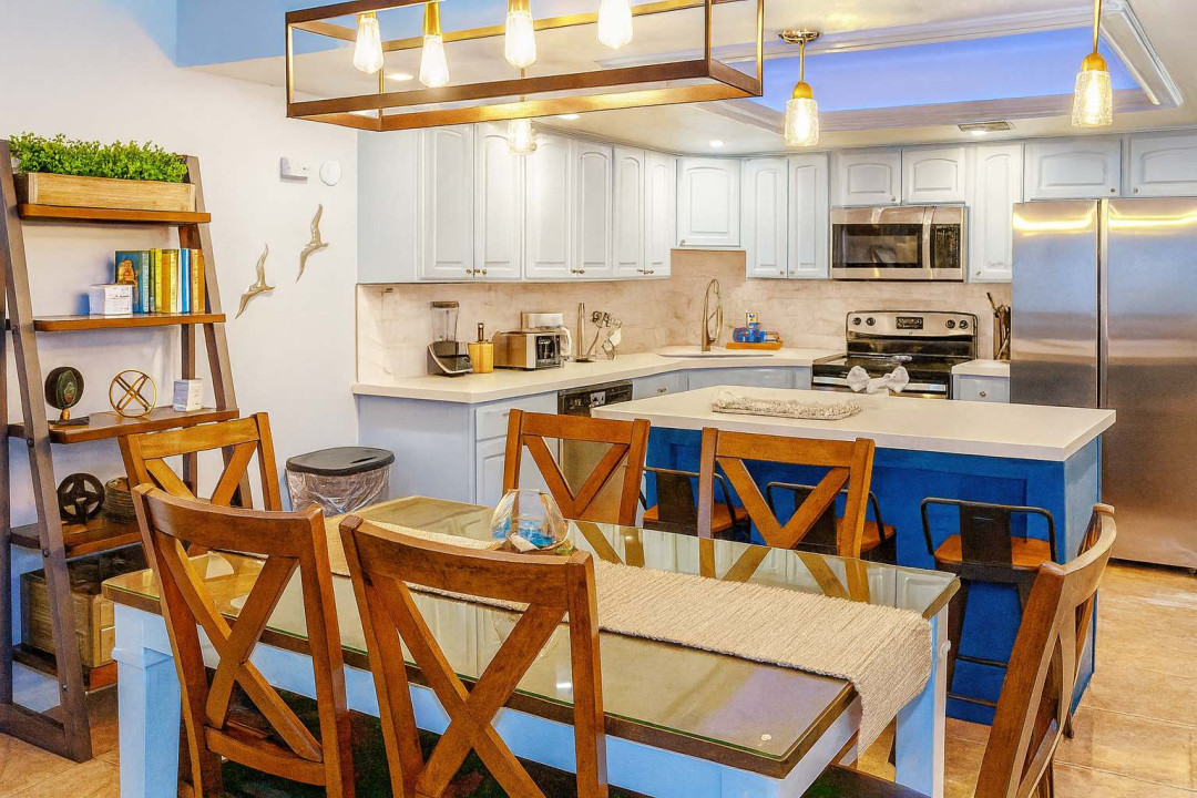 Modern Coastal Kitchen at Saida #3305
Sunlit open kitchen features crisp white cabinets, gleaming stainless steel appliances, striking navy quartz island seating 4-6. Rustic wood table, coastal shelves with greenery—ideal for beachy breakfasts.