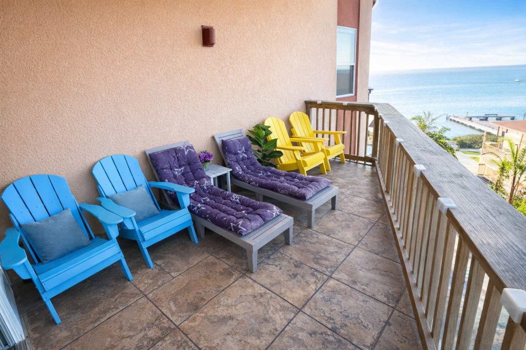 Relax on a spacious waterfront balcony with vibrant Adirondack chairs, plush loungers, and tropical views—perfect for morning coffee or sunset cocktails. Steps from the beach, ideal for couples or families seeking coastal charm.