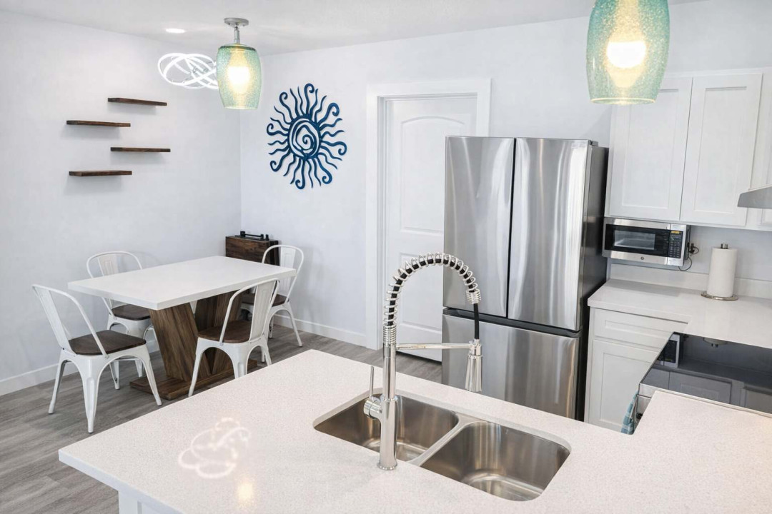 Bright Coastal Kitchen + Dining | Stylish Decor, Stainless Appliances, Blue Sun Accent, Floating Shelves, Modern Lighting, Family-Friendly Layout, Walk to Beach, Ideal for Couples or Small Groups