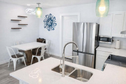 Bright Coastal Kitchen + Dining | Stylish Decor, Stainless Appliances, Blue Sun Accent, Floating Shelves, Modern Lighting, Family-Friendly Layout, Walk to Beach, Ideal for Couples or Small Groups