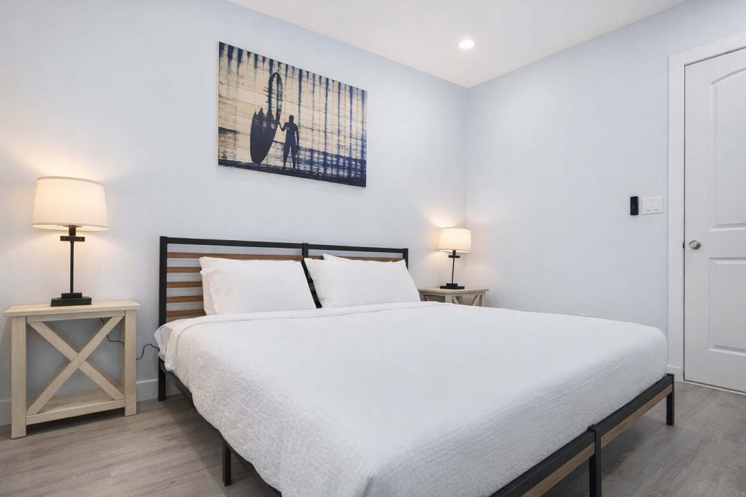 Modern Coastal Retreat | Steps from the Beach  
Relax in this stylish, sunlit bedroom featuring a minimalist design, plush white bedding, warm lighting, and serene wall art. Perfect for couples or solo travelers seeking comfort.