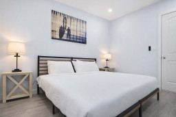 Modern Coastal Retreat | Steps from the Beach  
Relax in this stylish, sunlit bedroom featuring a minimalist design, plush white bedding, warm lighting, and serene wall art. Perfect for couples or solo travelers seeking comfort.
