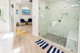 Coastal Chic Bathroom + Lounge | Steps to Beach
Bright spa-style shower with marble walls, pebble floor and glass enclosure. Includes vanity, striped mat and cozy lounge with beach décor—perfect for relaxing after sun and surf.