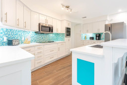 Bright Coastal Kitchen with Modern Appliances & Island
Enjoy cooking in this stylish coastal kitchen featuring white cabinetry, turquoise backsplash, stainless steel appliances & a spacious island with sink.