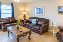 Luxurious Brown Leather Living Room
Plush leather sofas, marble-top coffee table, and accent chairs create a sophisticated lounge. Soft lighting, beach art, fresh flowers, and blue drapes add coastal elegance—perfect for relaxing.