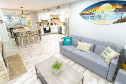 Unwind in a stylish, beach-inspired living space with plush seating, coastal decor, and an open layout. The nearby dining area and fully equipped kitchen make entertaining easy, while mirrored accents enhance the breezy, light-filled ambiance.