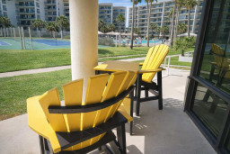 Sunny patio with resort views—tennis courts, pool, and palm-lined grounds just steps away. Relax in vibrant Adirondack chairs and soak up the South Padre Island vibe. Perfect for morning coffee or sunset lounging.