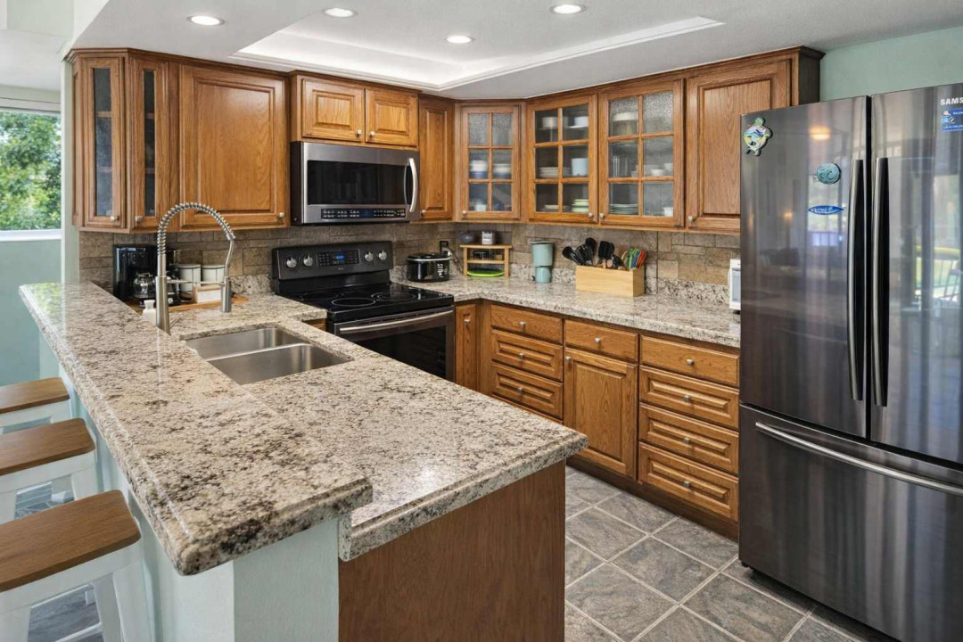 Modern U-Shaped Kitchen with Granite Counters, Stainless Appliances, Breakfast Bar, and Natural Wood Cabinetry — Perfect for Cooking & Casual Dining