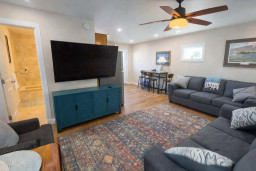 Cozy open-layout living room with smart TV, plush sofas, vibrant rug, and dining nook—steps from bathroom and natural light window. Ideal for relaxing, streaming, or sharing meals in a stylish, well-lit space.