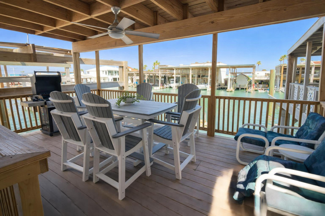 Waterfront deck with dining, lounge seating, ceiling fan, and canal views—perfect for grilling, relaxing, and entertaining in coastal comfort. Steps from boat slips and stilted beach homes.