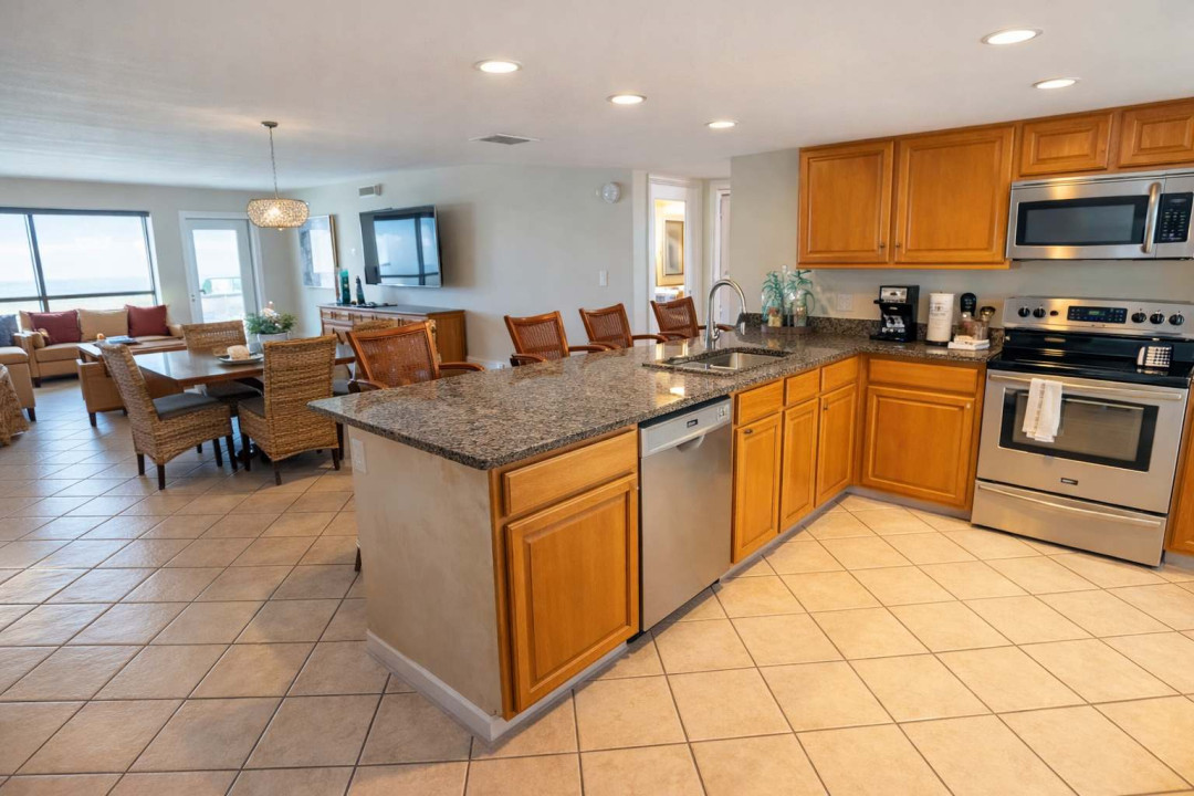Bright, open-concept kitchen and dining area with warm wood cabinetry, granite counters and stainless appliances. Natural light fills the space, flowing seamlessly into a cozy living zone—perfect for gatherings, family meals & relaxed coastal stays.