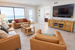 Sunlit coastal living room featuring caramel leather seating, a sleek entertainment console, and ocean views through glass doors. Bright, airy, and styled for comfort—perfect for relaxing after beach days or cozy evenings in your South Padre getaway.
